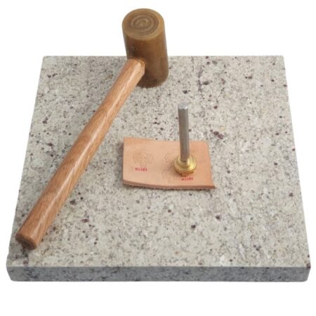 Granite tooling slab 300 x 300 mm with a mallet, leather stamp and piece of leather sitting on it.
